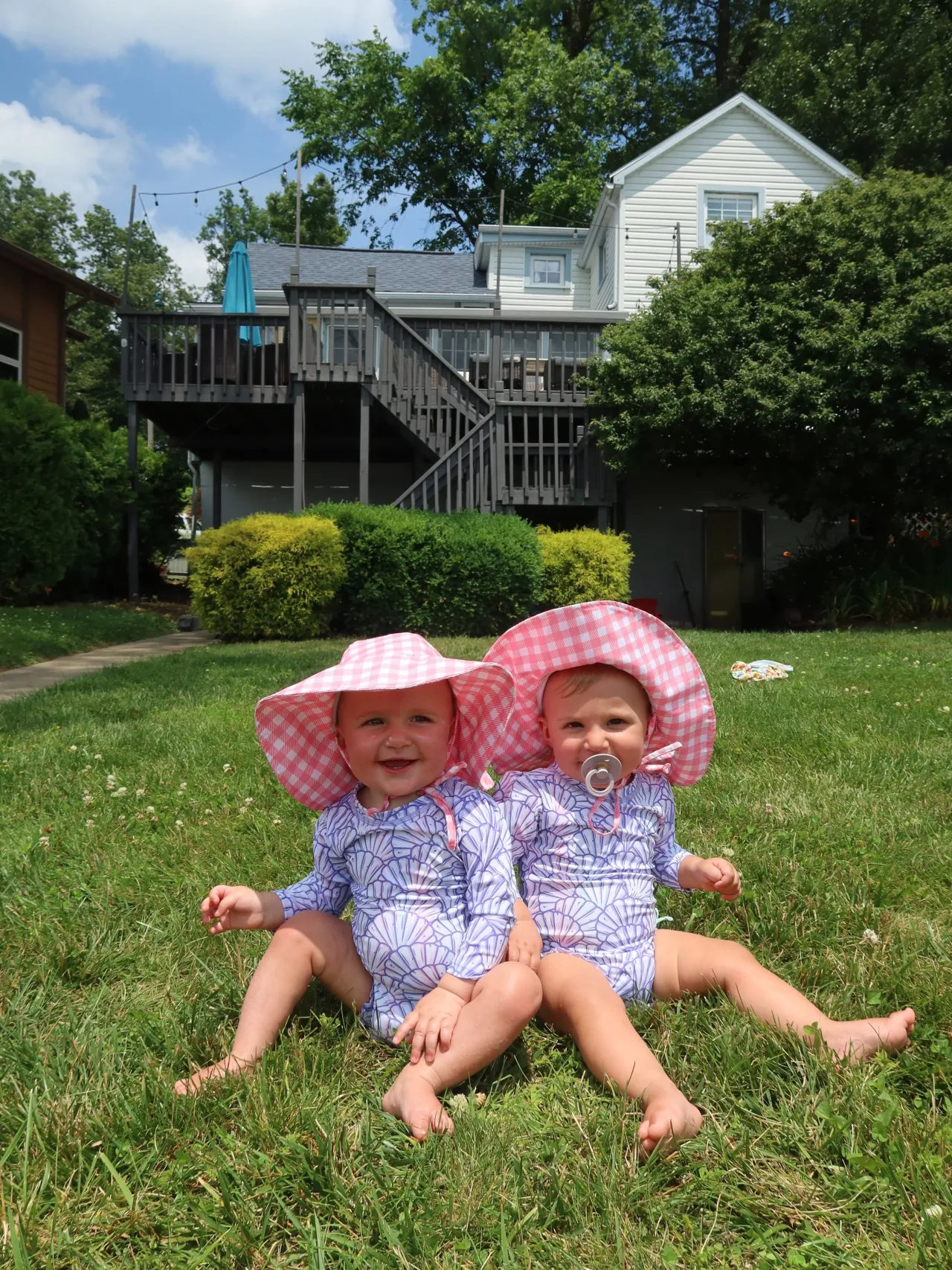 Two toddlers in sun hats sitting on the lawn in front of The Farmhouse