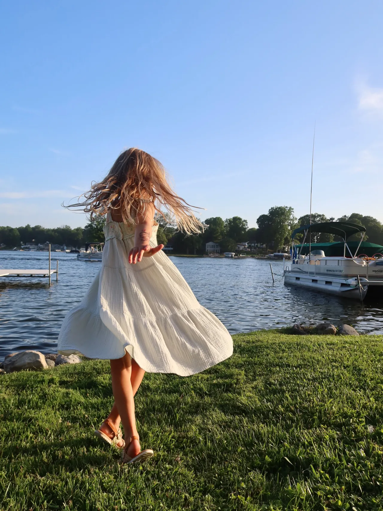 A girl twirling in a dress on the lakefront lawn at golden hour